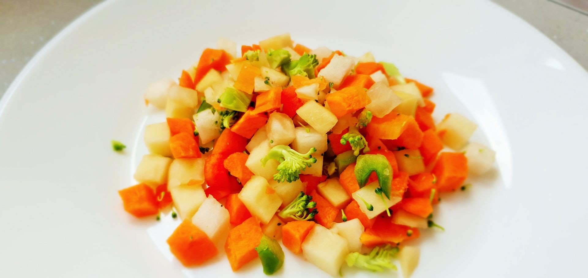 A plate of diced mixed vegetables including carrots, potatoes, and broccoli.