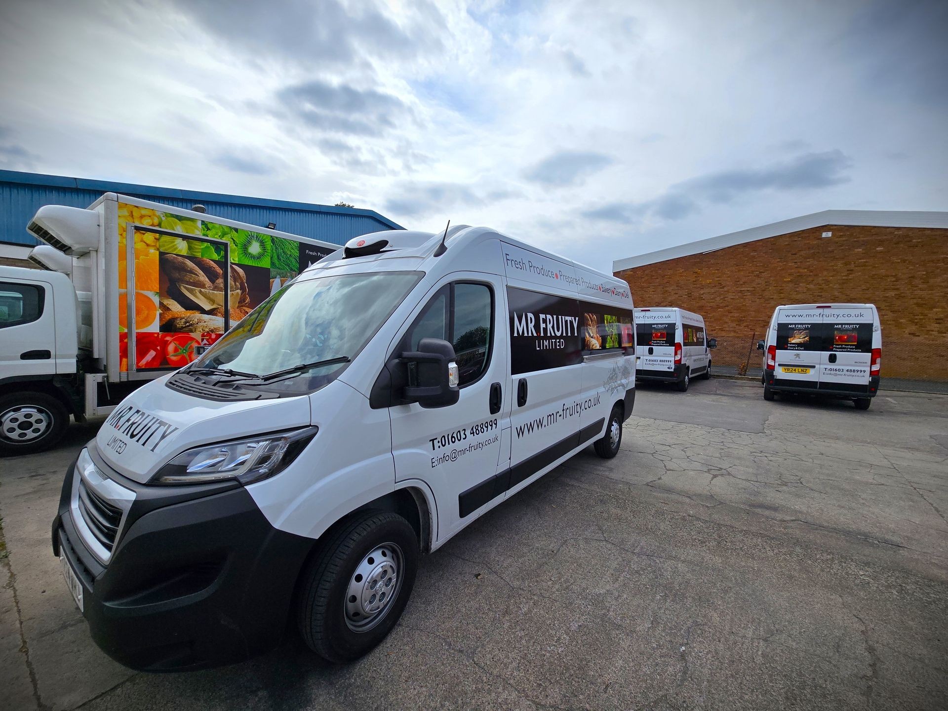 Fleet of Mr Fruity Limited delivery vans parked outside a warehouse with produce images on the sides.
